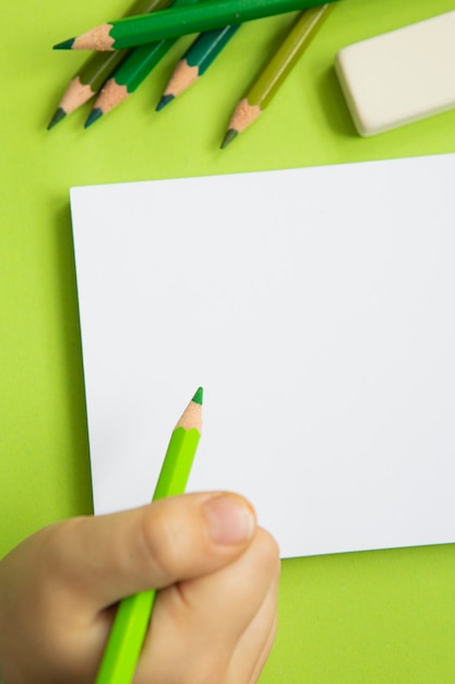 Blank page of a notebook on a green background and colored pencils