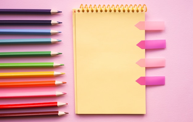 Blank page of vertical spiral sketching pad with crayons on pink 