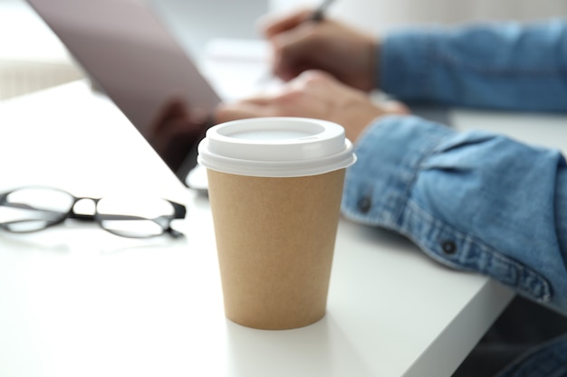 Blank paper cup against young man working on laptop.