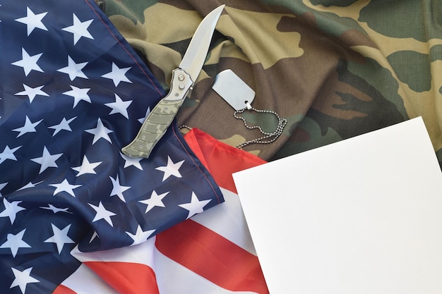 Blank paper lies with knife and army dog tag necklace on camouflage uniform and american flag