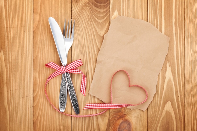 Blank paper for recipe or note and silverware on wooden table background