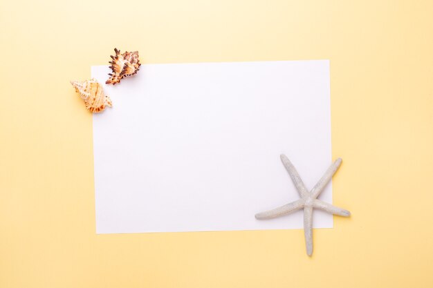 Blank paper, seashells and starfish on yellow background. Concept of planning summer holidays and vacation