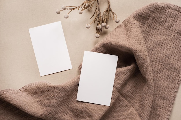 Blank paper sheet card with mockup copy space and dry floral branch and blanket cloth on neutral beige background Minimal aesthetic business brand template Flat lay top view