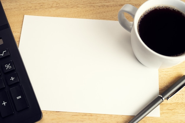 Blank paper on wooden desk table with cup of coffee and calculator. Mock up template. Economy, financial or business concept