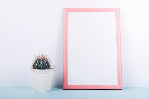 Blank photo frame with small succulent potted plant on blue table