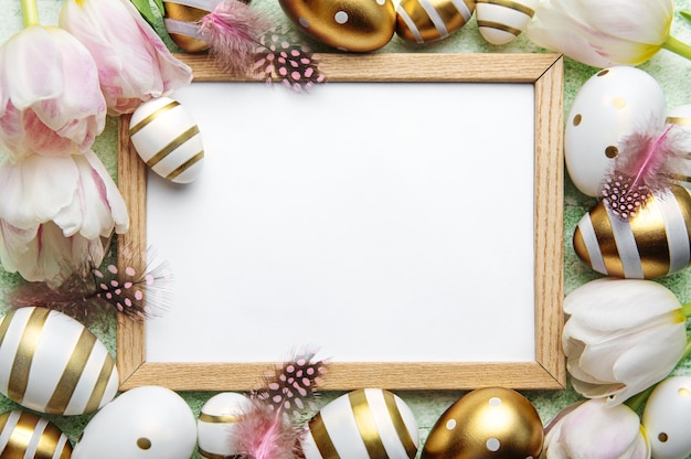 Blank picture frame surrounded by Easter eggs and tulip flowers on green background