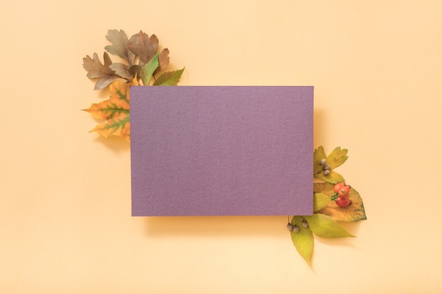 Blank purple greeting card or paper note with autumnal leaves, top view