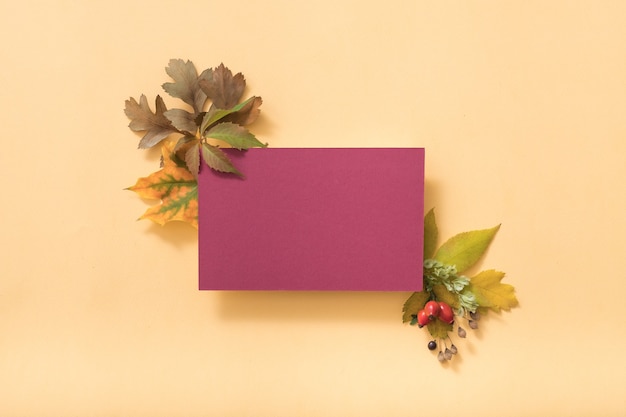 Blank purple greeting card or paper note with autumnal leaves, top view