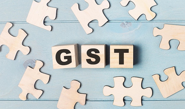 Blank puzzles and wooden cubes with the text GST Goods and Services Tax lie on a light blue background