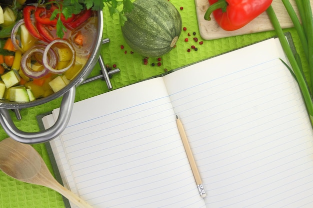 Blank recipe book with vegetable soup kitchen equipment and veggies around them