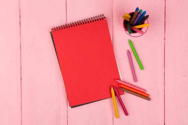 Blank red note pad and crayons on pink wooden table