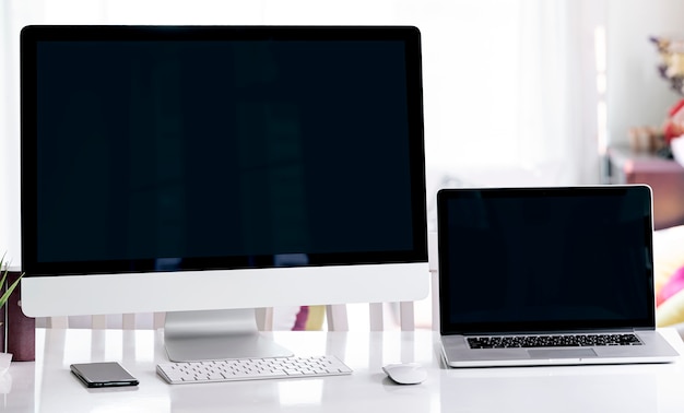 Blank screen desktop computer and laptop in minimal office room with decorations