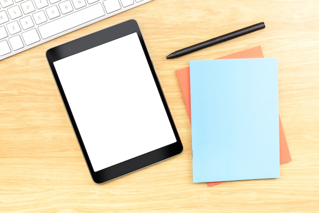 Blank screen mobile tablet with blue notebook and pen at wood table