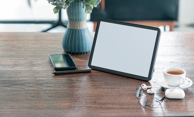 Blank screen tablet, gadget and coffee cup on wooden table in cafe room with copy space.