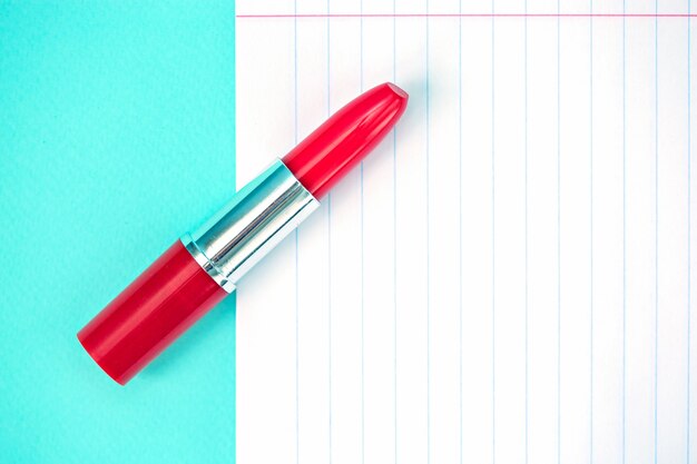 A blank sheet of notebook paper and red lipstick on a blue background.