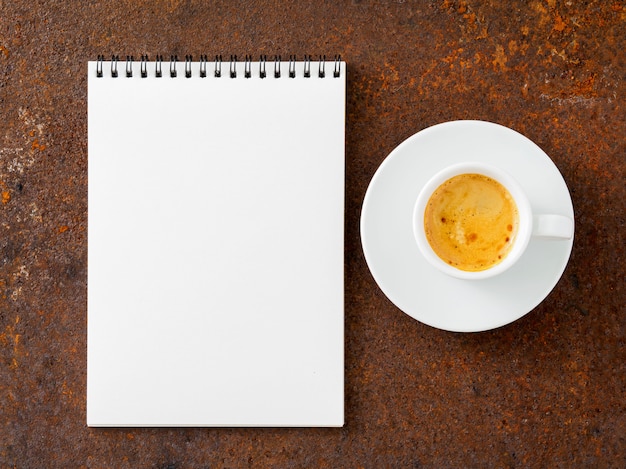 Blank sheet of notebook  a spiral and cup of coffee on rusted old iron table, top view.