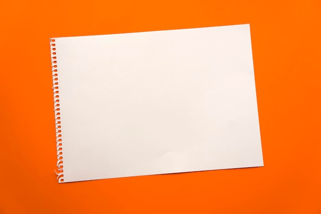 Blank sheet of paper space for design and lettering on a beautiful orange background A sheet of perforated paper torn from a notepad rests obliquely on the surface Square sheet of paper