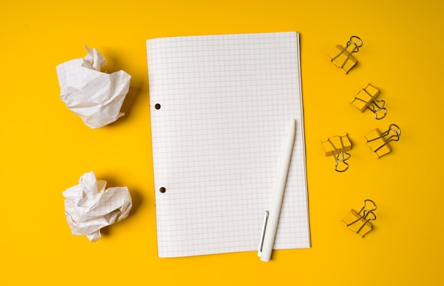 Blank spiral notebook and crumbled paper balls on yellow background