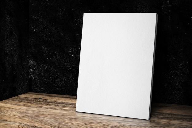 Blank white canvas frame leaning at grunge black stone wall and wood floor