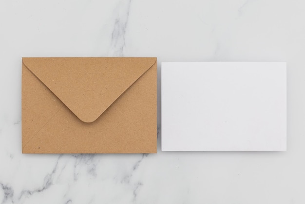 Blank white card with kraft brown paper envelope on marble background