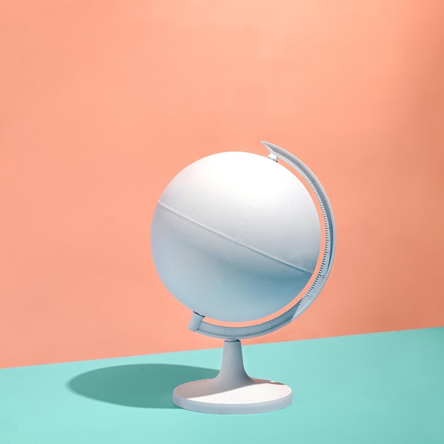 Blank white globe on a pedestal casting a shadow over a bicolor apricot or orange and green background with copy space in square format