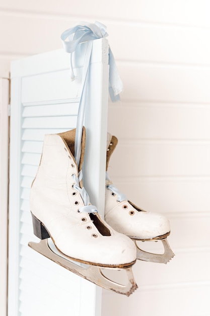 Blank white ice skates with blade and lace ribbon. Hang on blue shutters from window. concept of original Christmas decor. photo