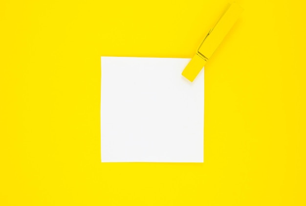 Blank white To Do List Sticker with yellow wooden clothespin. Close up of reminder note paper on the yellow background. Copy space. Minimalism, original and creative photo.