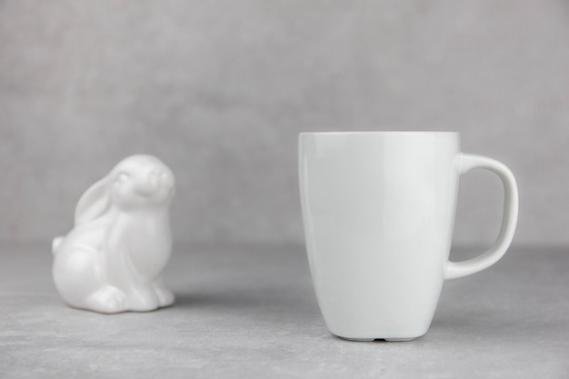 Photo blank white mug mockup with ceramic easter bunny on light gray concrete stone background spring composition side view copy space