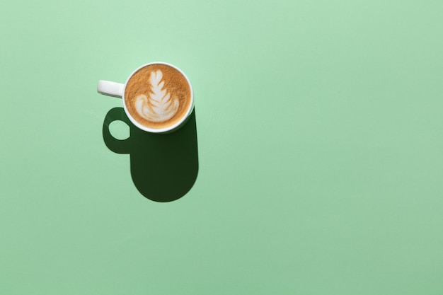 Blank white mug with cappuccino, latte art in hard light on pastel green table, top view