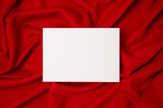 Blank white paper card on red fabric flat lay top view copy space wedding invitation card design