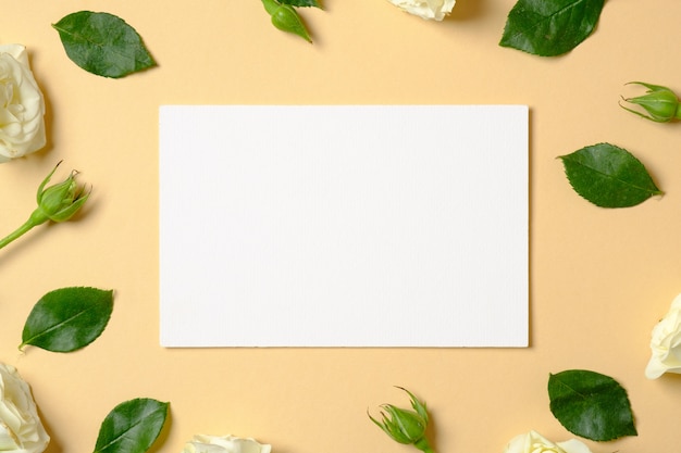 Blank white paper and frame made of roses flowers and green leaves