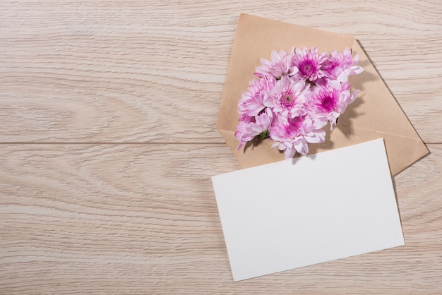 Blank white paper tag with brown envelope and pink flowers on wooden table.