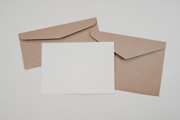 Blank white paper on the two brown paper envelope. Mock-up of horizontal blank greeting card. Top view of Craft paper envelope on white background. Flat lay of stationery.