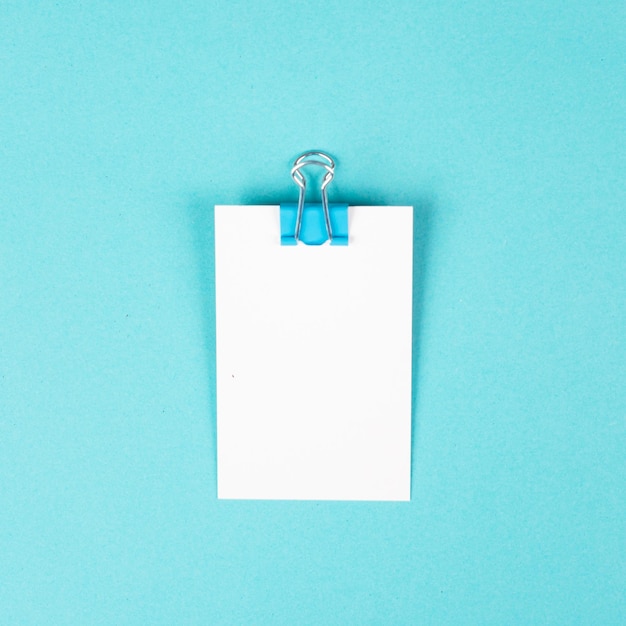 Blank white paper with a paperclip on a blue colored background, copy space for text, reminder