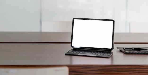 Blank white screen digital tablet with magic keyboard on wooden table in meeting room