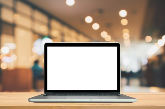 Blank white screen laptop computer on wood table top with cafe restaurant background