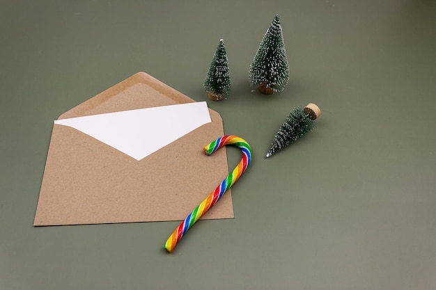 A blank white sheet in a craft envelope next to small Christmas trees. Mockup of invitation and greeting card. The style is modern minimalism. Top view, flat lay.