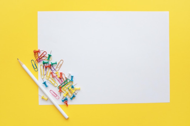 Blank white sheet of paper with a pencil multicolored paper clips and buttons