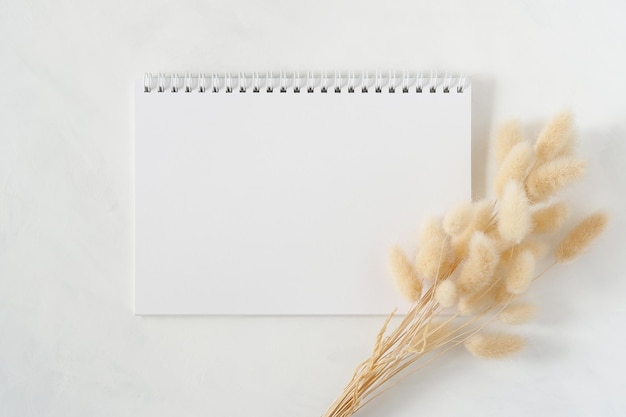 Blank white spiral notebook with natural dried bunny tail grass bouquet on white background