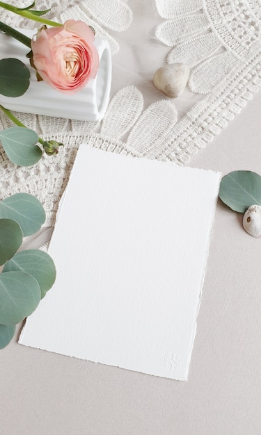 Blank white Wedding Greeting invitation card  silver eucalyptus leaves branch, blush pink buttercup ranunculus flower on textured paper table backgound. Elegant modern template Flat lay top view