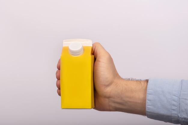 Blank yellow cardboard bag with cap in mans hand. Packet of juice or milk. mock up.