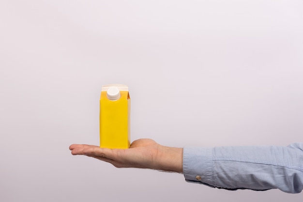 Blank yellow cardboard bag with cap on mens palm. Packet of juice or milk. mock up.