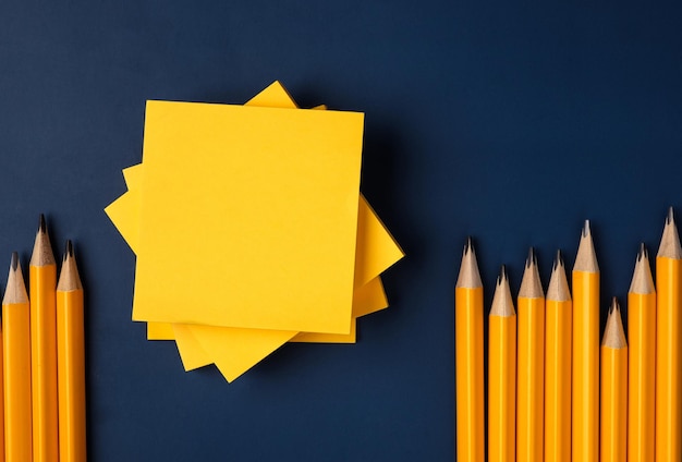 Blank yellow sticky note and pencil on navy blue table background