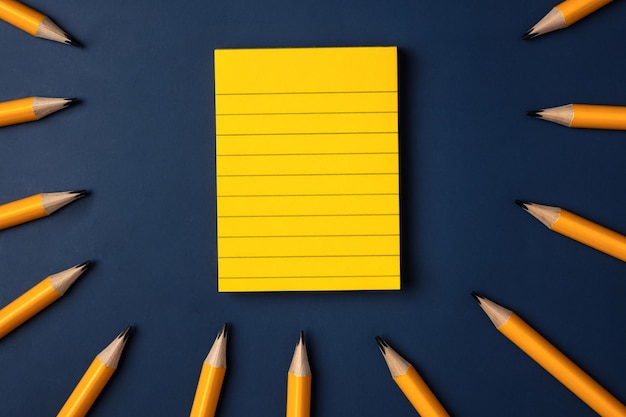 Blank yellow sticky note and pencil on navy blue table background