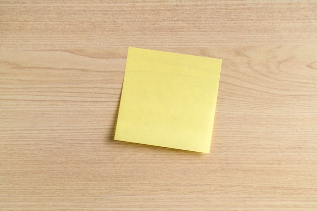 Blank yellow sticky note, post note on wooden office desk background. Copy space, mockup