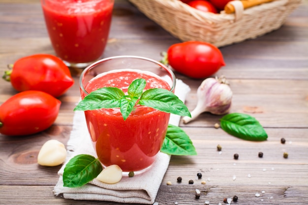 Blended fresh tomato juice with basil leaves in glasses on a napkin  on a wooden table