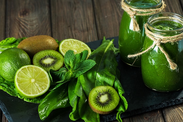 Blended green smoothie with ingredients on the stone board, wooden table