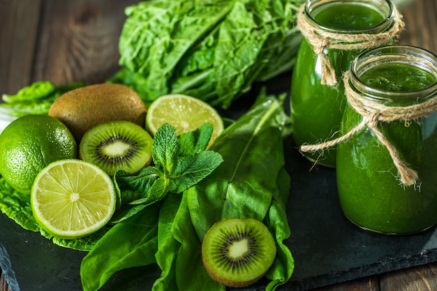 Blended green smoothie with ingredients on the stone board, wooden table