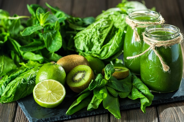 Blended green smoothie with ingredients on the stone board, wooden table