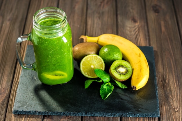 Blended green smoothie with ingredients on the stone wooden tabl